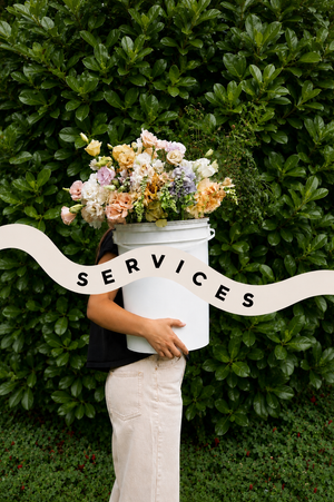 Person holding a white bucket with flowers against a green hedge, with 'SERVICES' banner in Vancouver BC