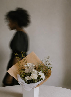 Bouquet of white flowers wrapped in brown paper on a white surface with a blurred figure in the background for funeral in Vancouver
